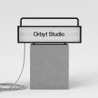 Billboard mockup featuring a rectangular illuminated sign displaying Orbyt Studio mounted on a concrete base with a coiled cable, ideal for graphic designers.