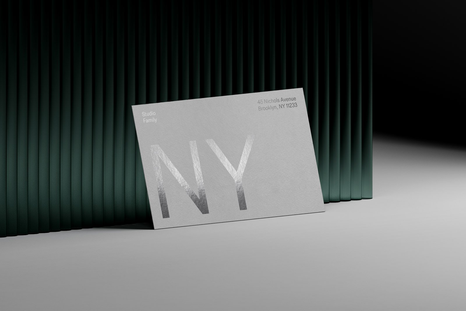 Business card mockup with silver foil text placed against a dark green, vertical pleated background in a minimal studio setup for print mockup designs.
