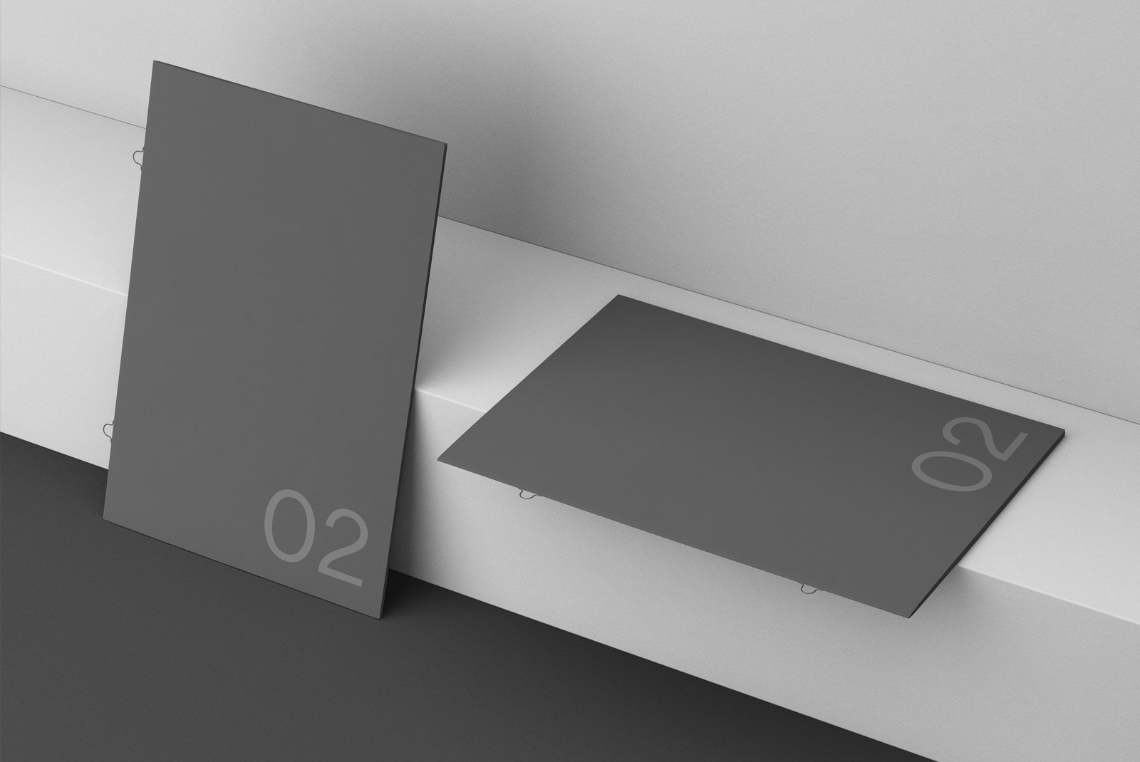 Two dark grey poster mockups leaning and laying on a white surface with the number 02. Perfect for graphic designers creating print or billboard mockups.