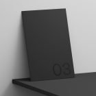 Minimalist black print mockup featuring a booklet with number 03 leaning on a black shelf. Ideal for graphic designers seeking sleek print design templates.