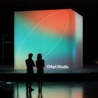 Digital billboard mockup with colorful gradient background displaying Orbyt Studio. Two people standing in front. Perfect for graphic and billboard designers.