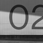 Large number 02 on an industrial corrugated metal wall under sunlight shadow ideal for billboard mockups outdoor graphic design and architectural presentations