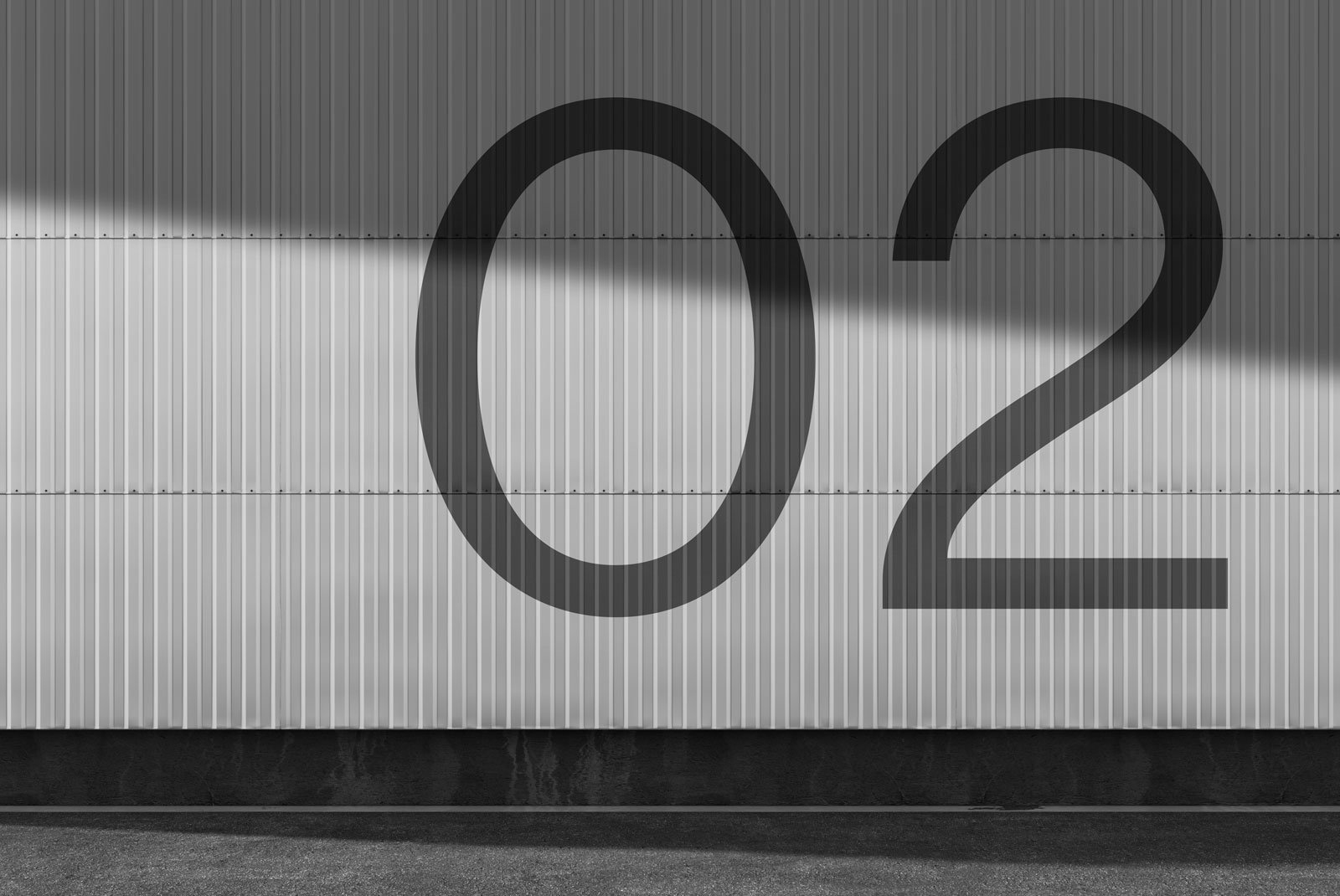 Large number 02 on an industrial corrugated metal wall under sunlight shadow ideal for billboard mockups outdoor graphic design and architectural presentations