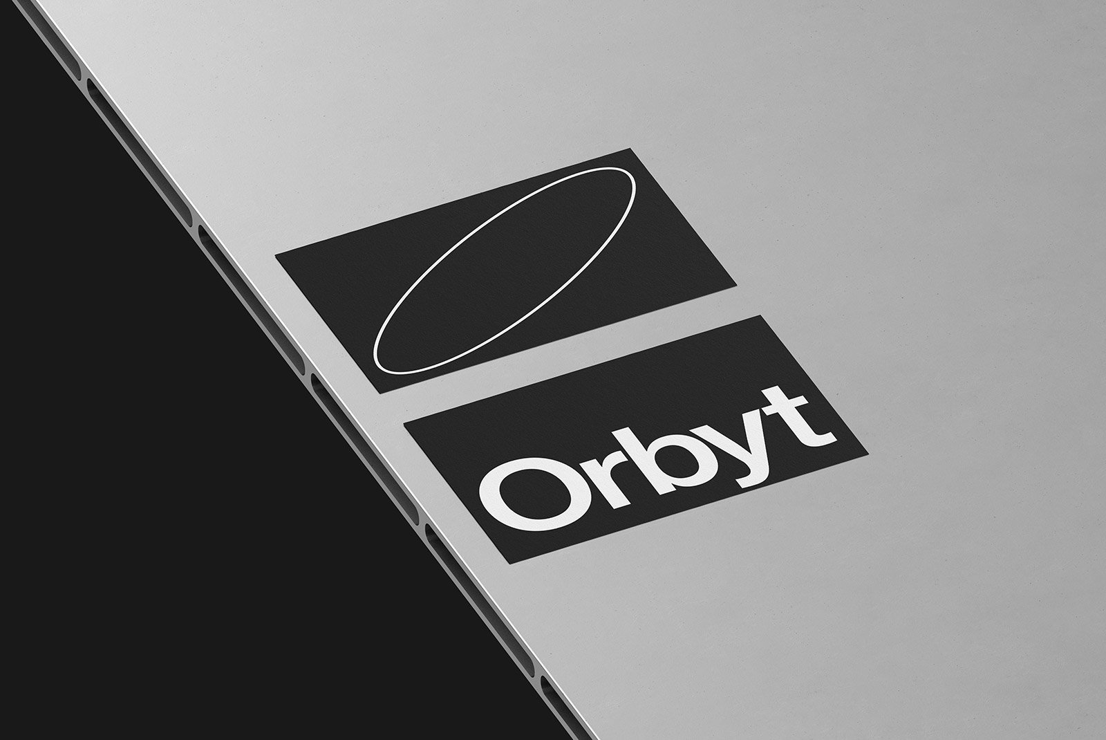 Tech mockup showing a laptop's edge with two black stickers featuring modern text and graphics. Suitable for branding and promotional packaging mockups.