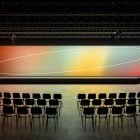 Empty conference room with colorful gradient screen stage and black chairs ideal for billboard mockups and presentation designs suitable for graphic designers