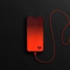 Smartphone tech mockup featuring a black phone with a red gradient screen and red charging cable on a dark background perfect for graphic designers
