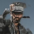 Blurry man with beard and sunglasses wearing a military-style hat and jacket captured in motion glitch effect. Perfect for graphic design use. Photoshop effects.