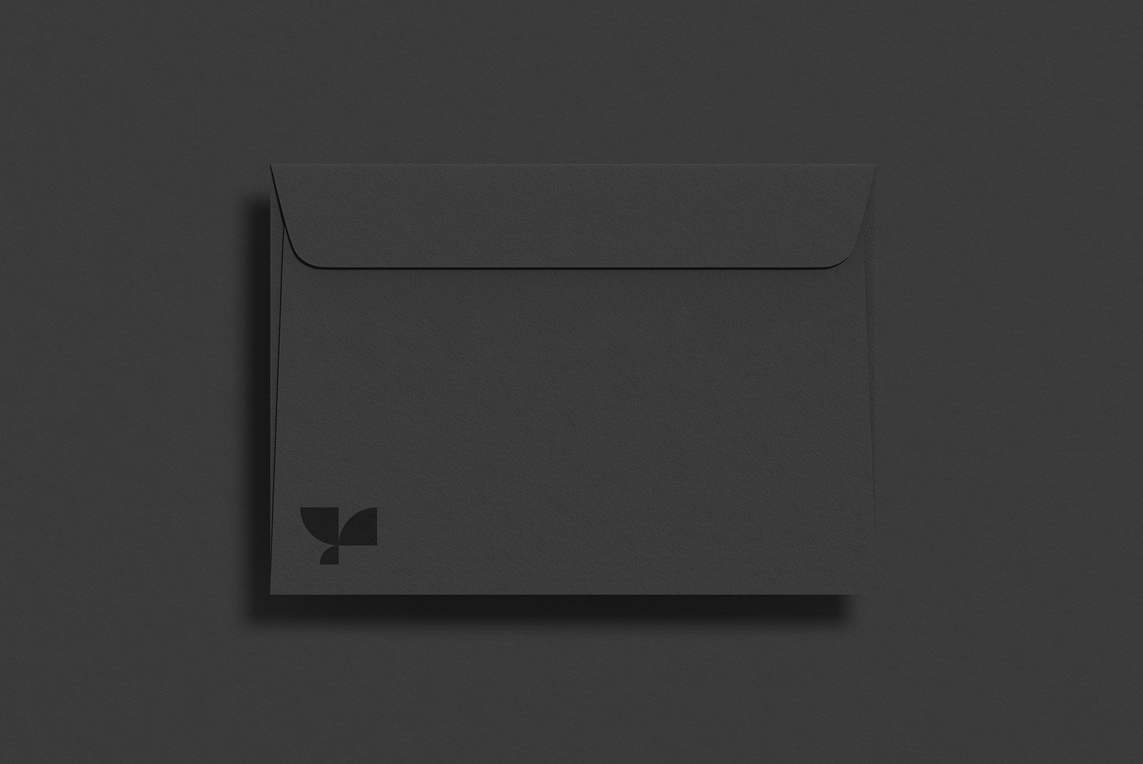 Black envelope on a dark background ideal for graphic designers. Suitable for packaging mockups. Minimalistic design with a small logo in the bottom corner.