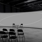 Modern tech mockup featuring a large curved screen in a dimly lit industrial setting with folding chairs arranged in rows and a table with two chairs in front