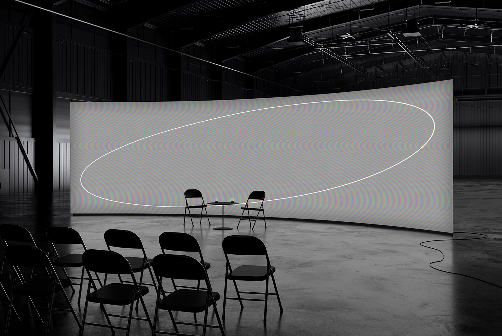 Modern tech mockup featuring a large curved screen in a dimly lit industrial setting with folding chairs arranged in rows and a table with two chairs in front