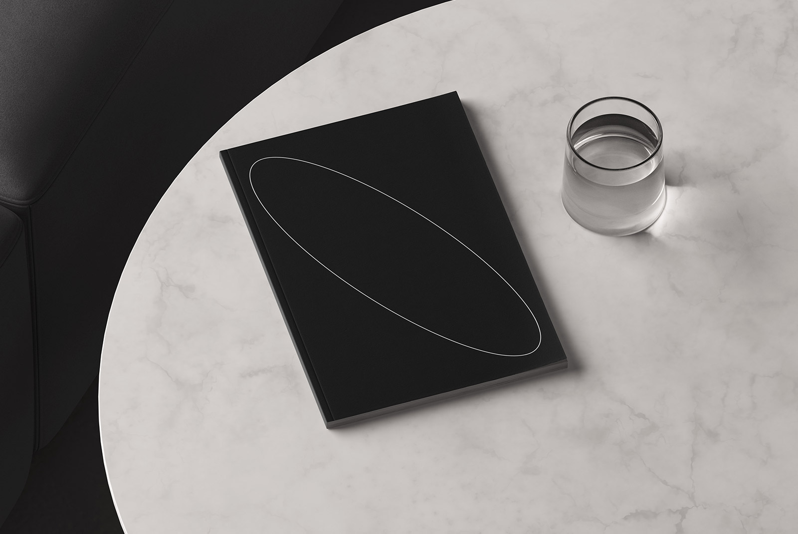 Black book cover mockup on a marble table near a glass of water ideal for graphic designers print mockups packaging mockups template design digital assets