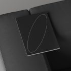 Top view of a minimalistic black hardcover book mockup with a white elliptical design, resting on a gray sofa. Ideal for print and graphic design projects.